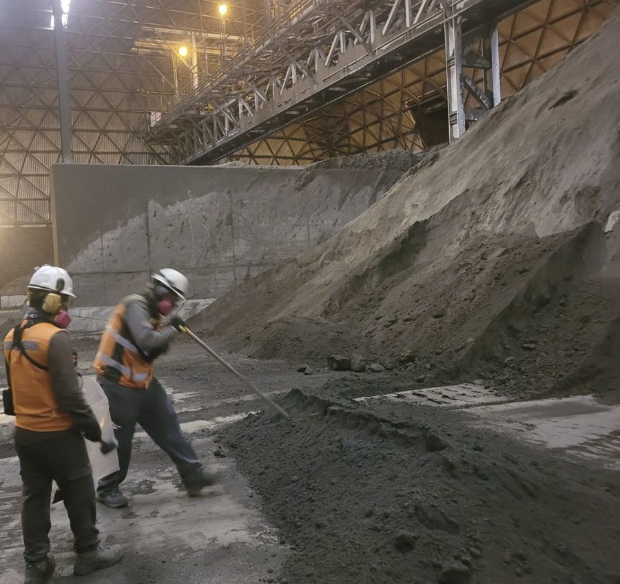 Two workers in protective gear beside a concentrate stockpile inside a shed